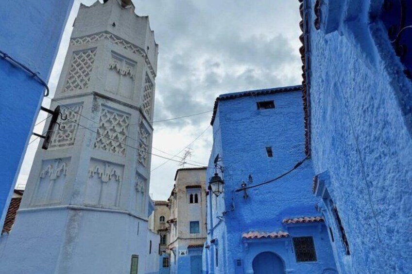 A narrow street with buildings painted in blue, a white tower with intricate carvings, and a clear sky. 2