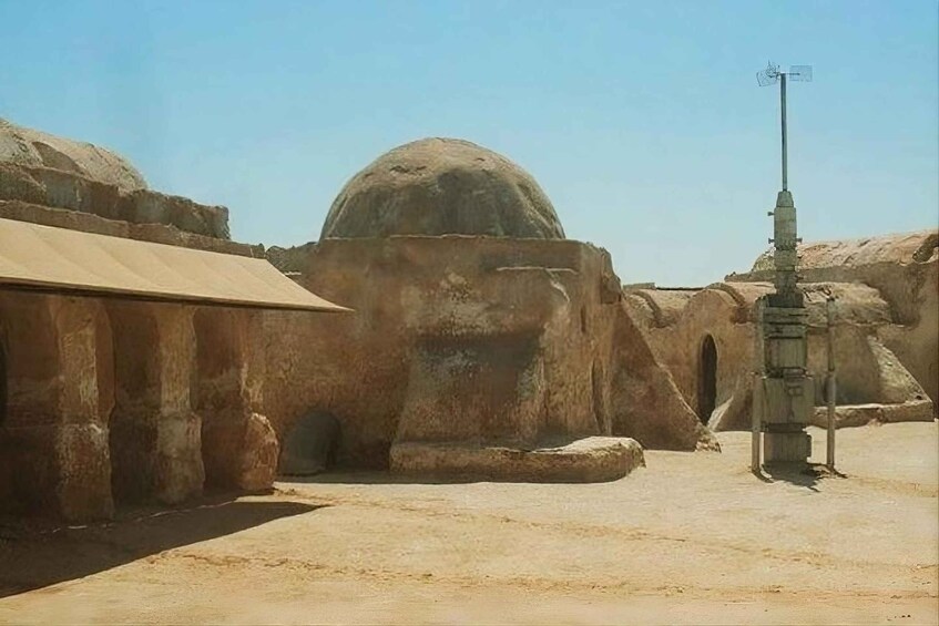 A desert landscape with a large rock formation, a dome-like structure, and a weather station. 3