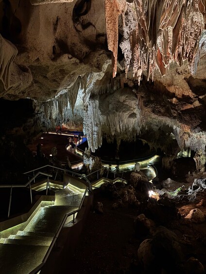 A cave with stalactites and stalagmites, illuminated walkways, and a pool. 3