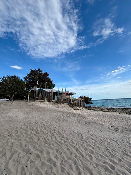 A sandy beach with a wooden structure and flags, trees, and a clear blue sky. 5