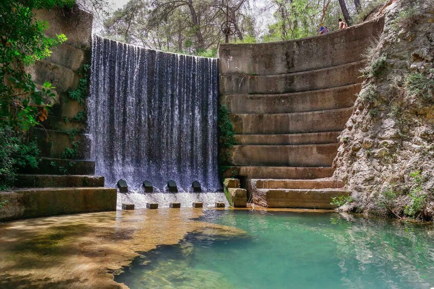 A waterfall cascading into a clear pool surrounded by stone steps and greenery. 5