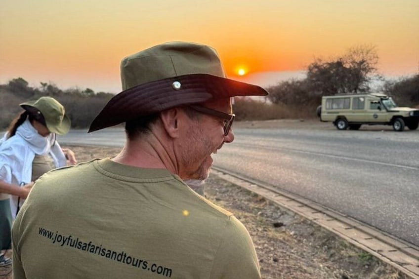 Una persona con sombrero y gafas de sol, un vehículo y un atardecer. 2