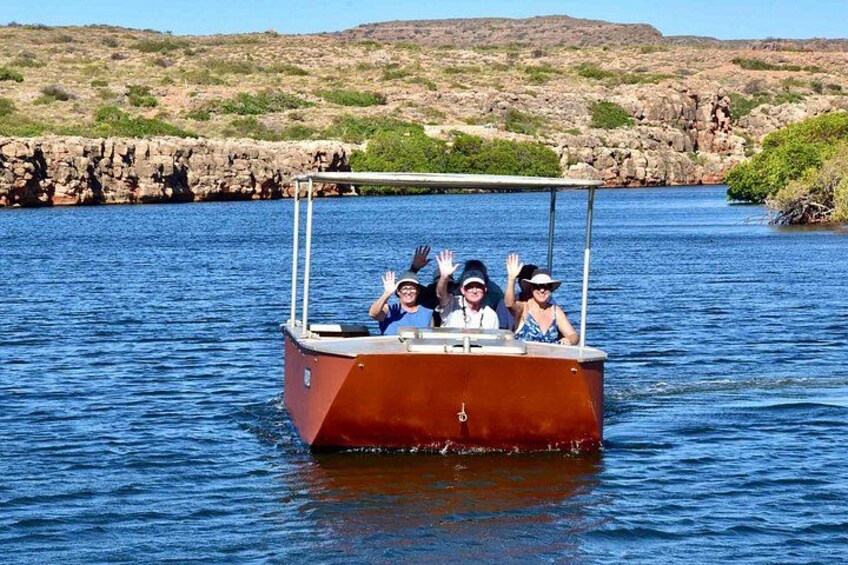 A boat with people on a calm body of water, surrounded by rocky terrain and sparse vegetation. 2