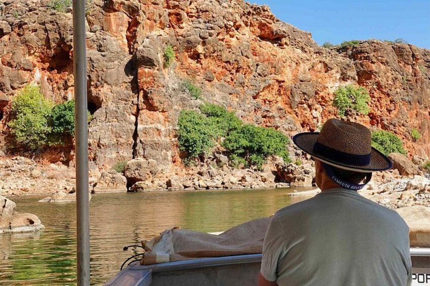A person in a boat with a rocky cliff and greenery in the background. 1