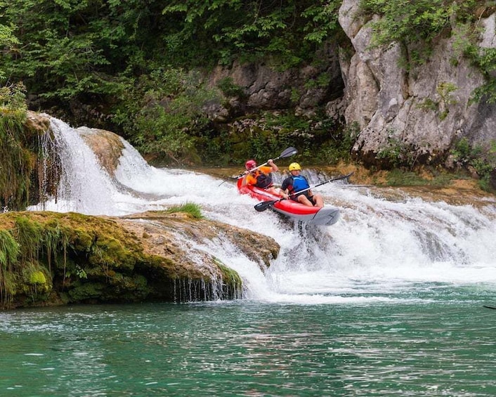 A person kayaking on a river with a waterfall. 1