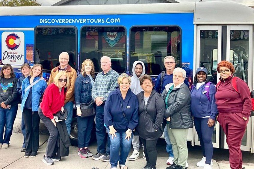 Eine Gruppe von Personen steht vor einem blauen Bus mit dem Text 'DISCOVERDENVERTOURS.COM' und einem Logo. 3