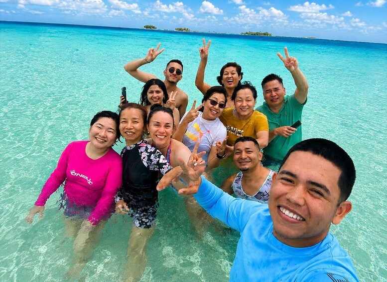 A group of people posing in clear turquoise water with a tropical island in the background. 1