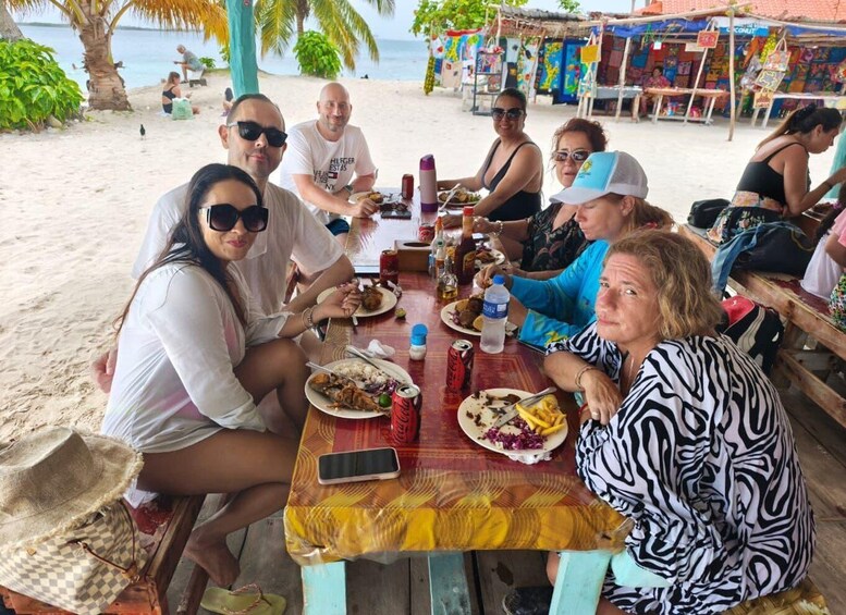 A group of people dining at a beachside table with various dishes and drinks. 3