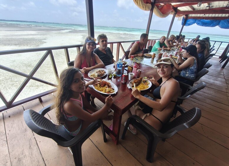 A group of people dining at a wooden table with a view of the beach and ocean. 5