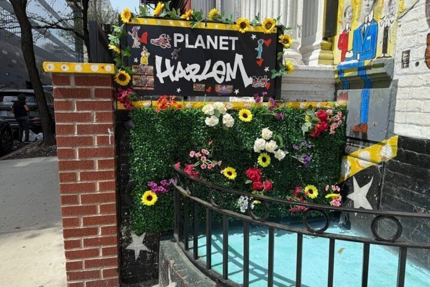 A sign for 'Planet Harlem' with a floral backdrop and a brick pillar. 5