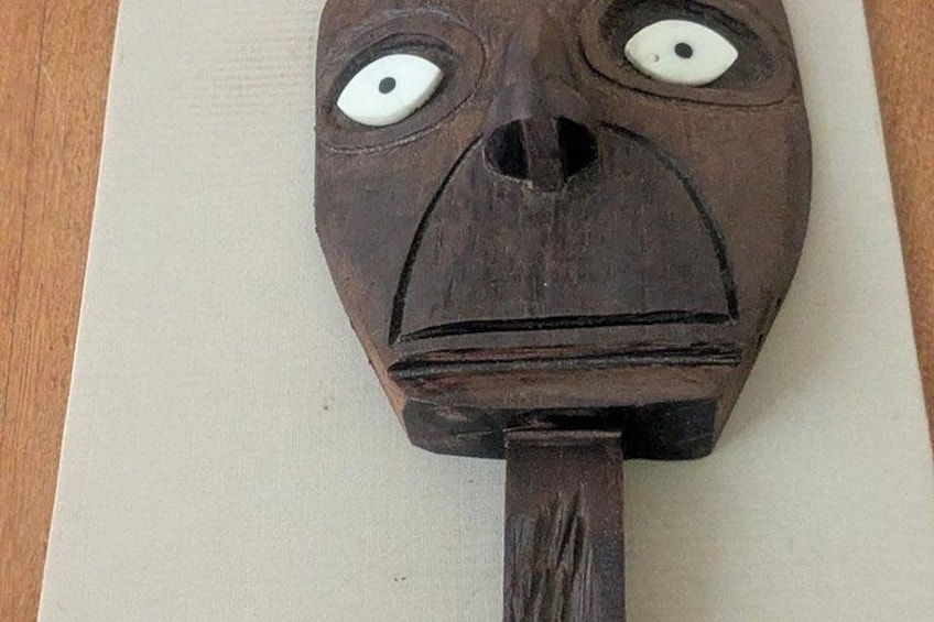 Een houten masker met uitgesproken gezichtskenmerken, waaronder grote ogen en een opvallende neus. 4