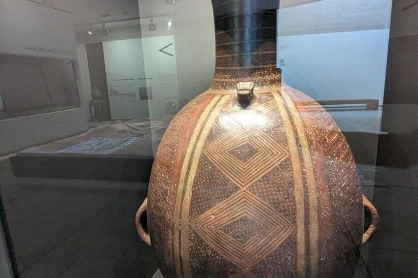 Een grote, versierde keramieken vaas met geometrische patronen, tentoongesteld in een museum. 3