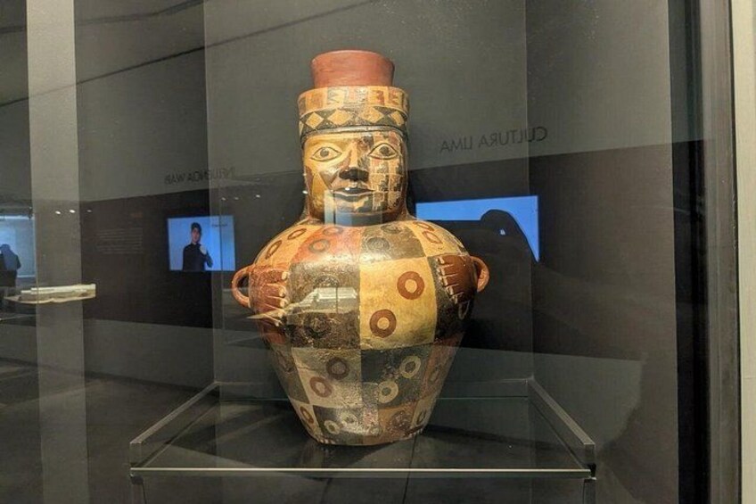 Een oud keramiek vaartuig met geometrische patronen en een menselijk gezicht, tentoongesteld in een museum. 2