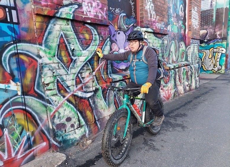 A person on a mountain bike with a colorful graffiti-covered wall in the background. 3
