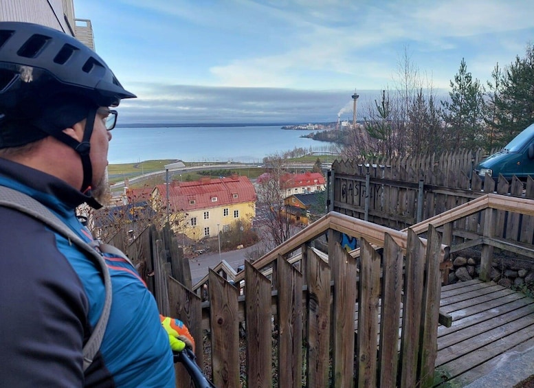 A person on a bicycle with a helmet, a wooden staircase, and a view of a body of water and buildings. 4