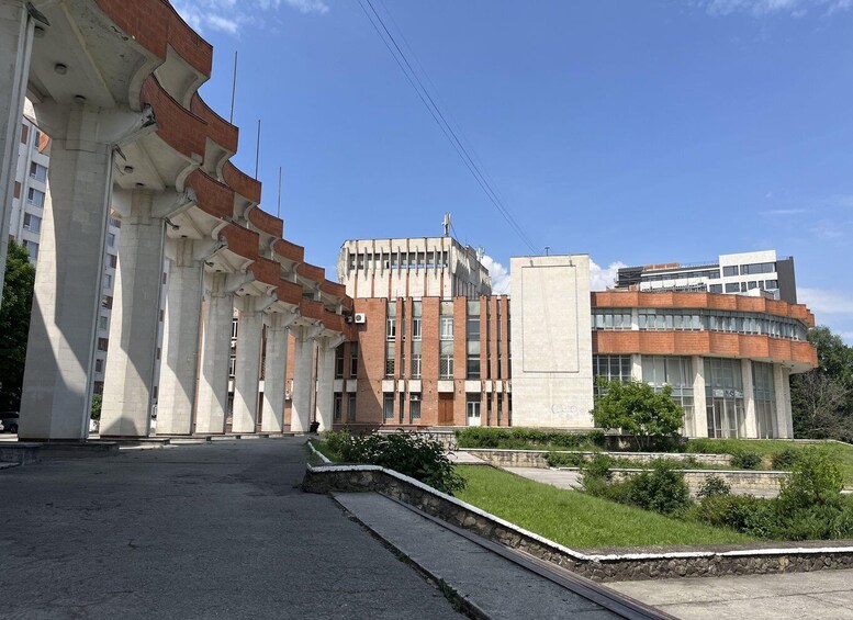 A modern building complex with a mix of brick and concrete architecture, a clear sky, and a paved pathway. 1