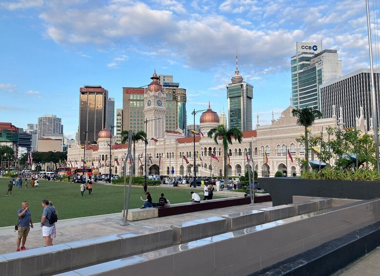 A cityscape with a prominent historic building, modern skyscrapers, and a public square with people. 1