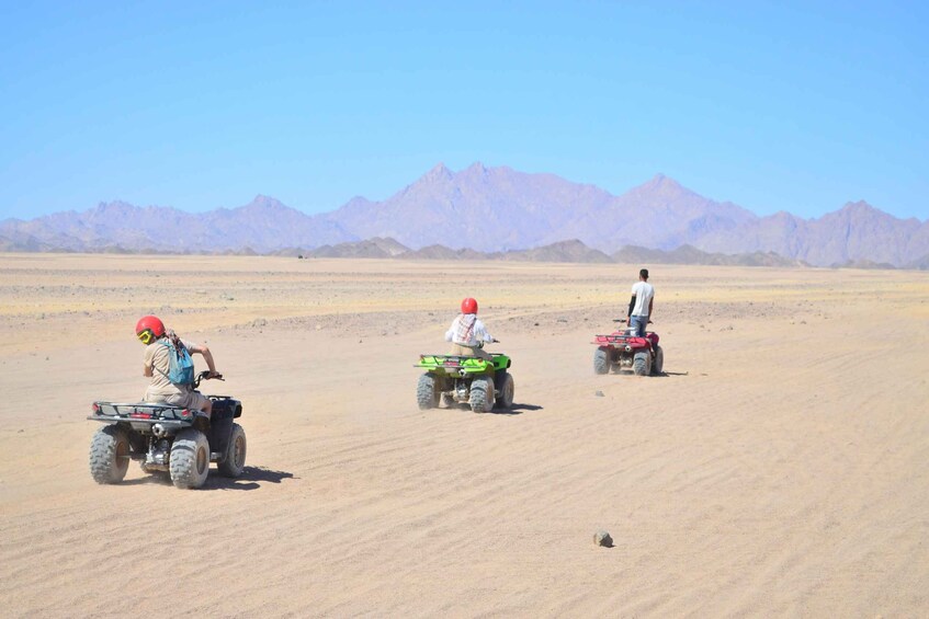 Three people riding ATVs in a desert with mountains in the background. 3