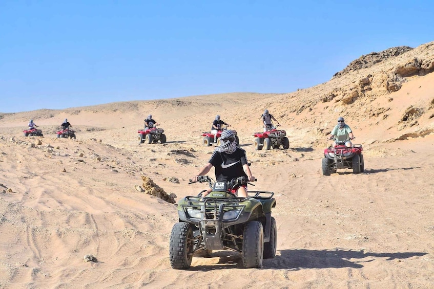 A group of people riding ATVs on a sandy terrain with hills in the background. 1