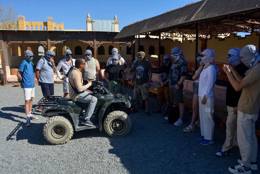 A group of people standing around a parked quad bike in an outdoor setting with a building in the background. 5