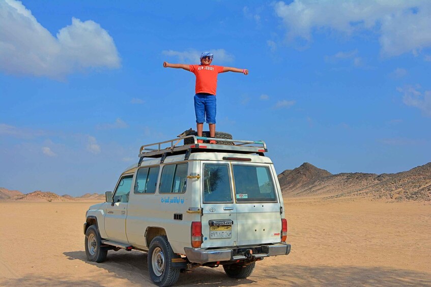 A person standing on the roof of a vehicle in a desert landscape. 1