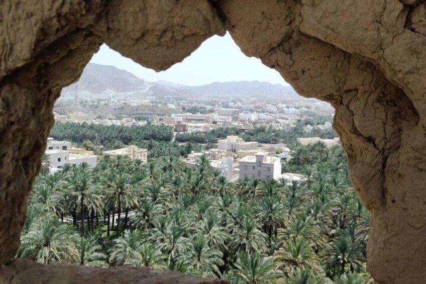 Vista a través de un arco de roca de un paisaje urbano con palmeras y montañas distantes. 5