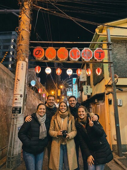 A group of people posing in front of illuminated signs and lanterns in a narrow street at night. 2