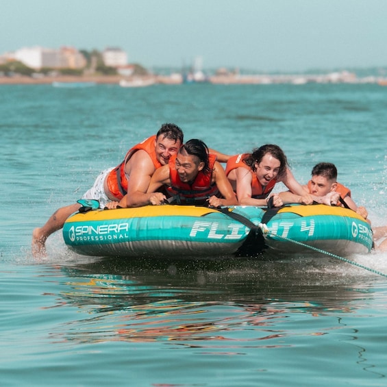 Four people on a tandem inflatable raft with 'SPINERA PROFESSIONAL' branding, moving through turquoise water. 1