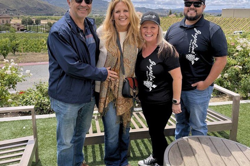 A group of people standing on a wooden deck with a vineyard in the background. 5