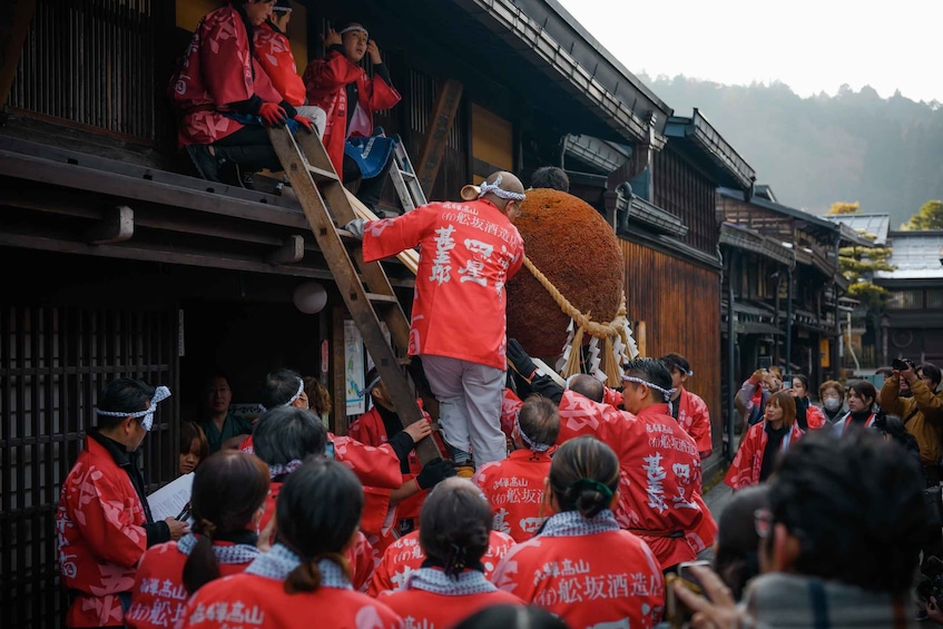 A group of people in red jackets carrying a large, round object on a wooden structure. 5