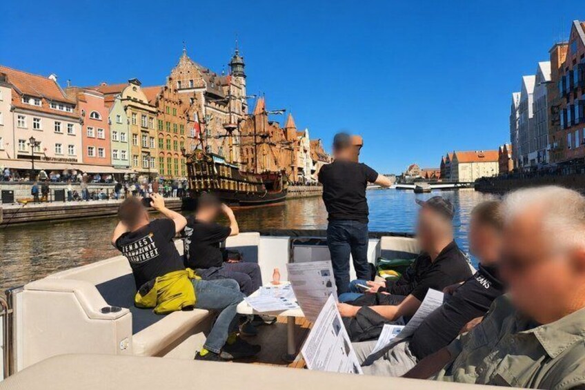 A boat tour with passengers enjoying the view of historic buildings and a tall ship. 3