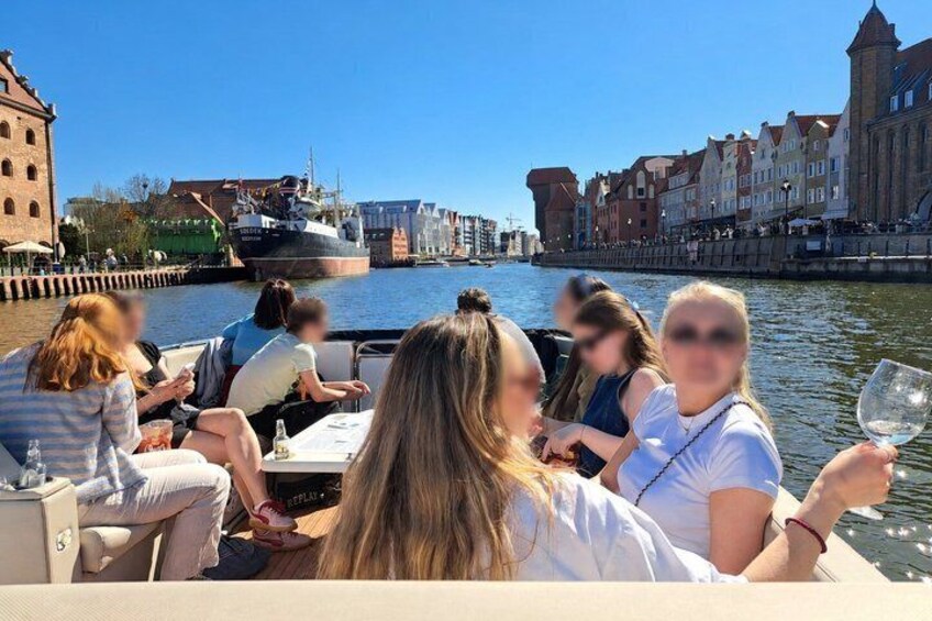 A group of people on a boat, a river, and historic buildings in the background. 1