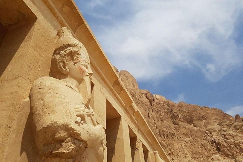 Une grande statue de pierre représentant un pharaon, tenant un bâton recourbé et un fléau, dressée sur fond de paysage désertique avec un ciel dégagé. 3
