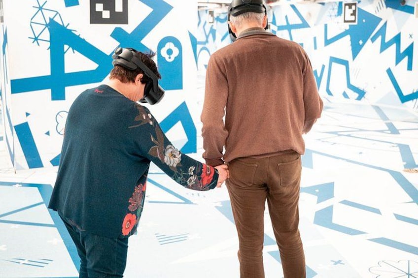 Two people interacting in an indoor setting with a geometric patterned wall. 1