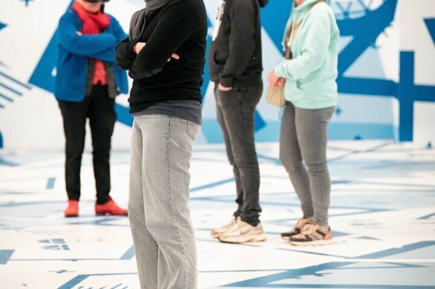 People standing in an outdoor area with a large blue and white geometric design on the ground. 5