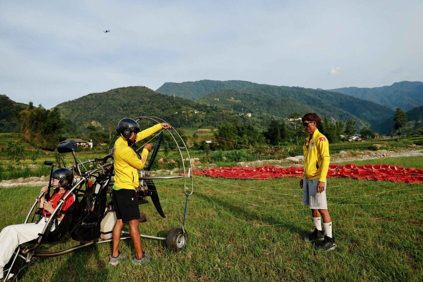 A glider with two pilots and a passenger on a grassy field with mountains in the background. 5