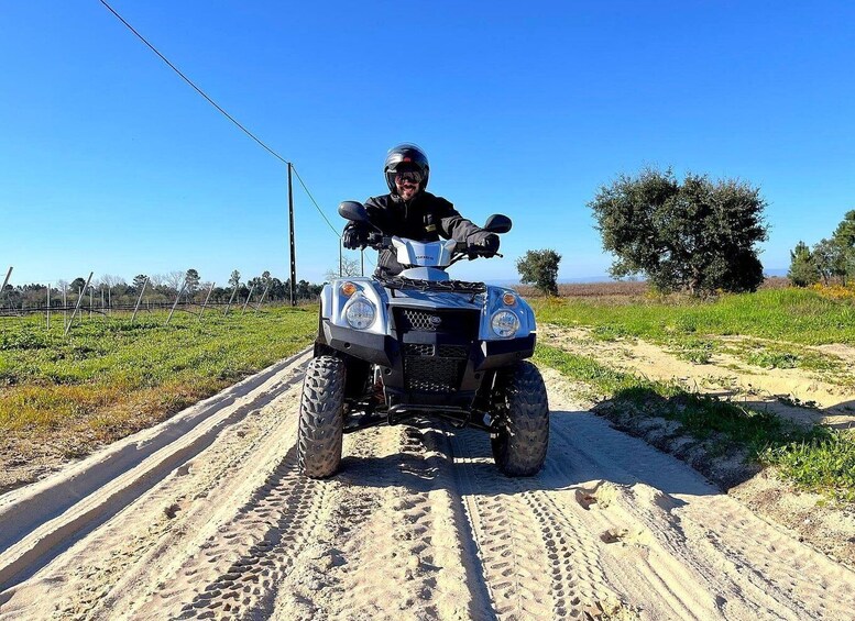 A person on a quad bike on a dirt path with green fields and trees in the background. 2