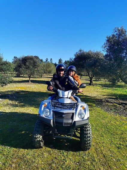 Two people on a quad bike in a grassy field with trees in the background. 3