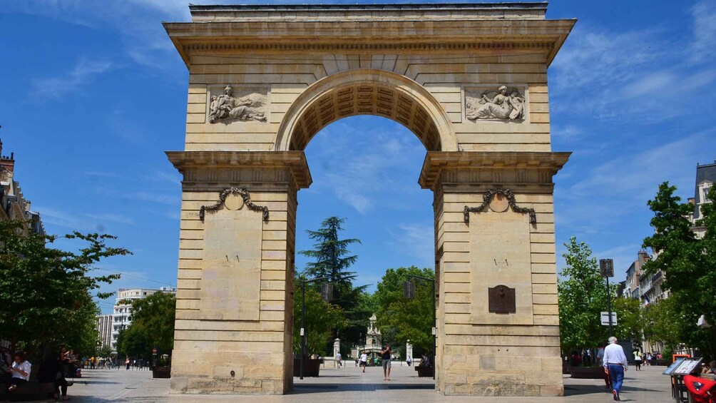 A large stone archway with classical sculptures, surrounded by trees and buildings. 2
