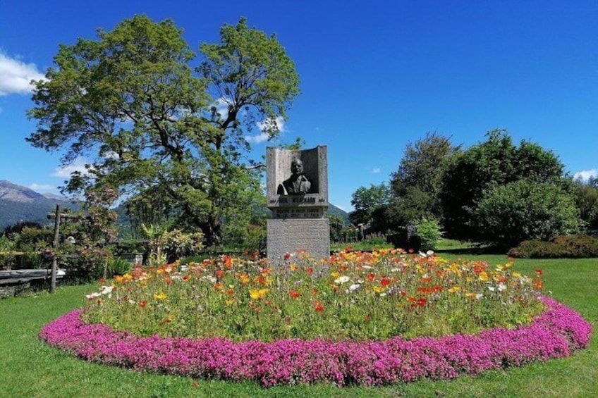 A statue surrounded by a flower bed with a mountain in the background. 1