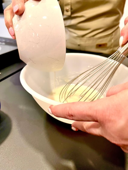 A person pouring a liquid into a bowl with a whisk. 3