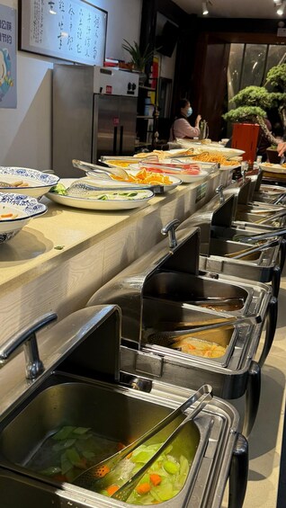 A buffet line with various dishes and a sink with vegetables. 1