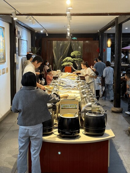 A buffet line with various dishes and pots, a clock on the wall, and a bonsai tree in the background. 2