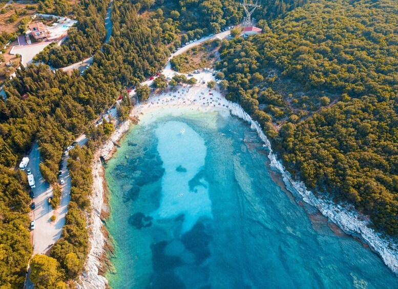 An aerial view of a coastal area with a beach, clear blue waters, and dense forested areas. 2