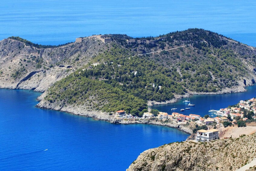 A coastal town with a fortified hill, clear blue sea, and boats anchored near the shore. 4