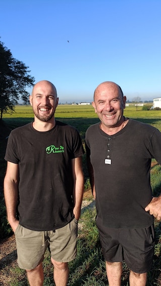 Two men standing outdoors, one wearing a black t-shirt with a logo and the other in a dark long-sleeve shirt. 2
