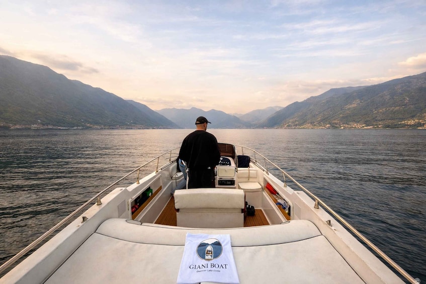 A boat with a man steering, surrounded by calm water and mountains. 3