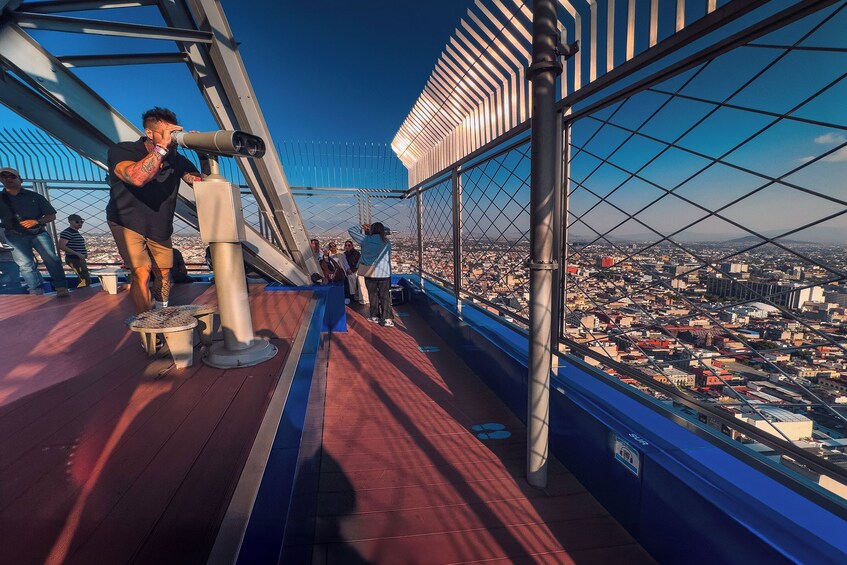 Una persona usando un telescopio sobre un puente con vista a un paisaje urbano. 5