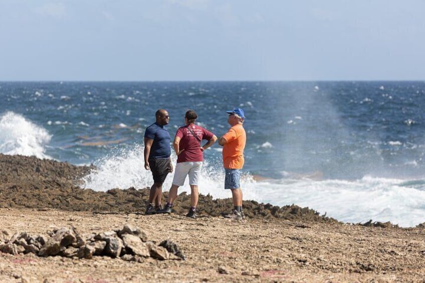 Drei Personen stehen auf einem felsigen Strand, während Wellen an die Küste branden. 3