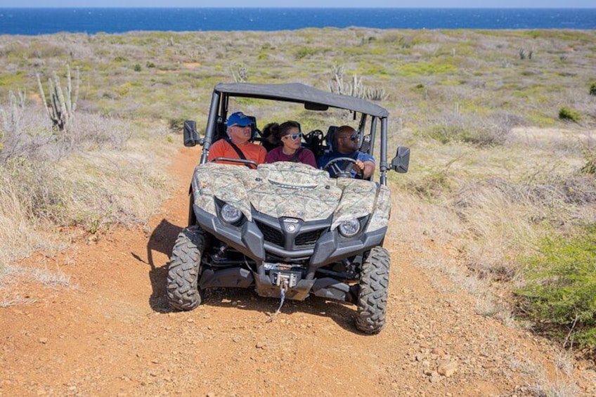 Un SUV de cuatro puertas en un camino de tierra, con un paisaje desértico y un cuerpo de agua al fondo. 1